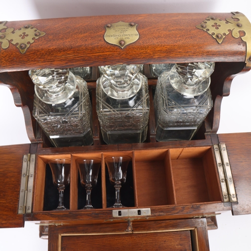 61 - A Victorian oak tantalus with 3 square cut-glass decanters, fold-out lids enclosing 3 liqueur glasse... 