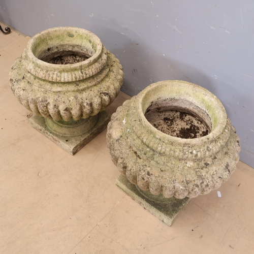 3029 - A pair of weathered reconstituted stone ovoid garden urns with excessive gadrooning on square bases.... 