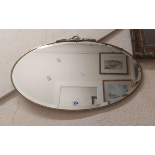 354 - A vintage brass framed bevelled oval wall mirror with cast pediment