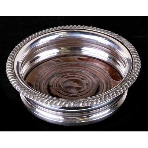 964 - A silver wine bottle coaster with turned wooden base. 15cm (6 ins) diameter