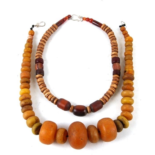 989 - An ethnic synthetic amber bead necklace; together with another similar, the largest 52cms (excluding... 