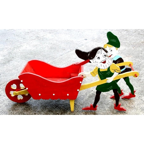 35 - A novelty painted wooden wheelbarrow being pushed by two gnomes, 97cms (38ins) long.