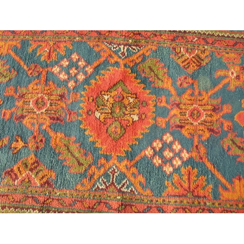 235 - A Turkish hand knotted woollen runner with repeated floral motifs on a blue ground within a multi bo... 