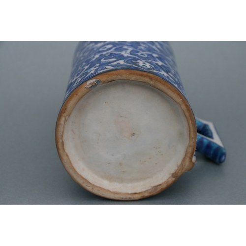 809 - A Turkish / Iznik pottery tankard decorated with foliate scrolls on a blue ground, 21cms high.