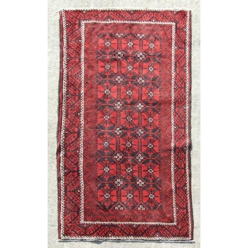 112 - A Persian Baluch woollen hand made rug with repeated guls within a stylised border, on a red ground,... 