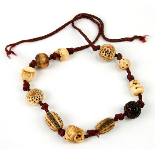 573 - A Japanese necklace of eleven ivory ojime beads to include a signed daruma, a skull, two bells and s... 