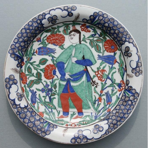 603 - A Turkish / Iznik shallow dish decorated with a figure amongst flowering foliage, 31cms diameter.