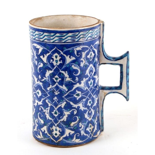 614 - A Turkish / Iznik pottery tankard decorated with foliate scrolls on a blue ground, 21cms high.