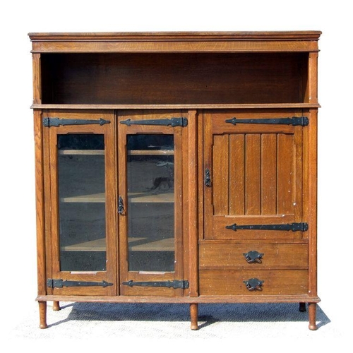 681 - An Arts & Crafts oak side cabinet, the pair of glazed doors enclosing a shelved interior flanked... 