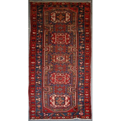 96 - A Persian Azari hand knotted woollen runner with five stylised guls within floral borders, on a blue... 