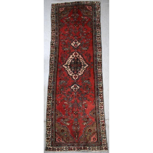 97 - A Persian Hamadan hand knotted woollen runner with central motif within a stylised border on a red g... 