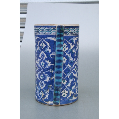 614 - A Turkish / Iznik pottery tankard decorated with foliate scrolls on a blue ground, 21cms high.