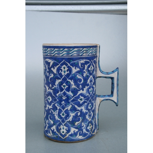 614 - A Turkish / Iznik pottery tankard decorated with foliate scrolls on a blue ground, 21cms high.