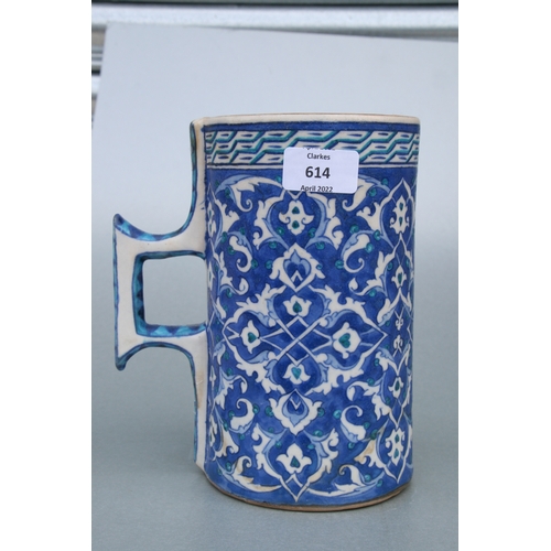 614 - A Turkish / Iznik pottery tankard decorated with foliate scrolls on a blue ground, 21cms high.