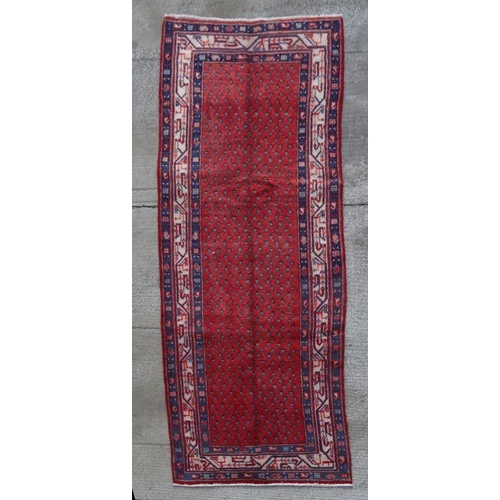 166 - A Persian woollen hand knotted runner with repeating motifs within stylised borders, on a red ground... 