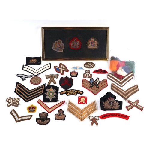 98 - A collection of cloth military shoulder titles and badges for various regiments and ranks.