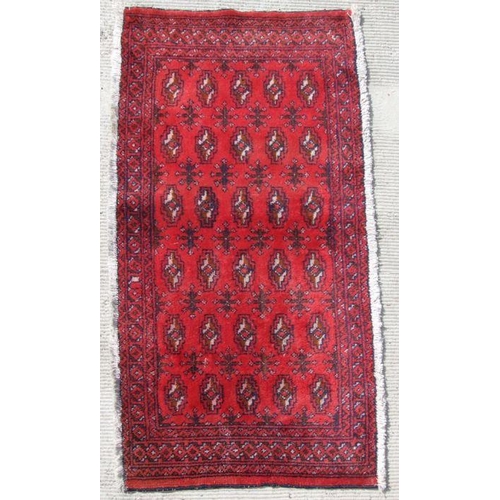 180 - A small Persian Turkoman rug with repeated guls on a red ground, 130 by 59cms.