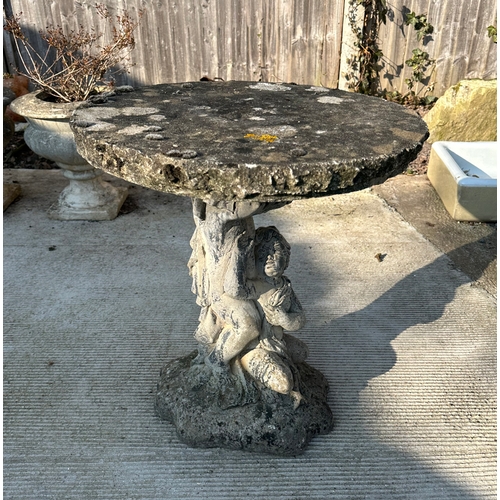 6 - A reconstituted stone bird table with circular top, on a cast cherub form support, 50cms dimeter.