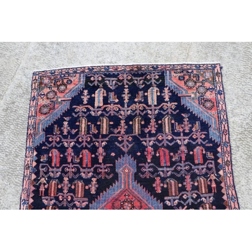 141 - A Persian hand knotted rug with stylised design, on a blue ground, 183 by 110cms (68).