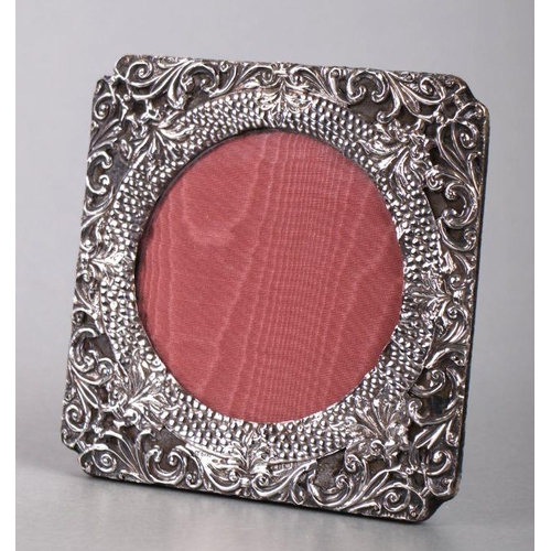 496 - An Edwardian silver strut photo frame with scroll decoration, Birmingham 1904, 15cms square.