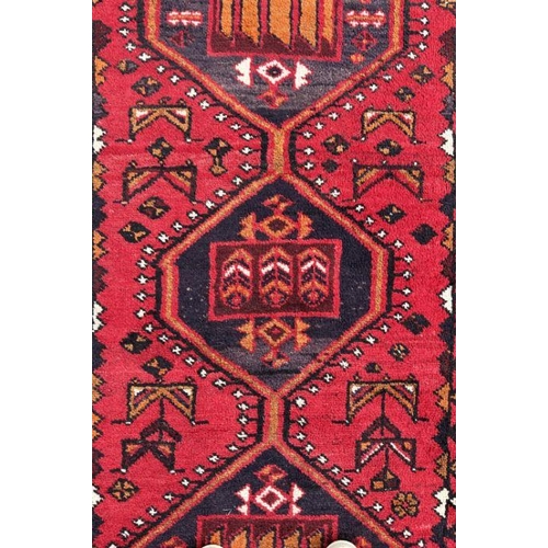 132 - A Persian rug with three central guls on a red ground, 148 by 240cms.