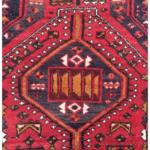 132 - A Persian rug with three central guls on a red ground, 148 by 240cms.