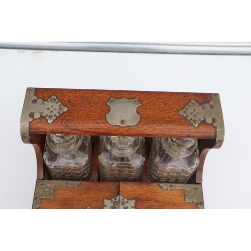 342 - A late 19th century oak three bottle Tantalus, the front section opening to reveal compartments cont... 