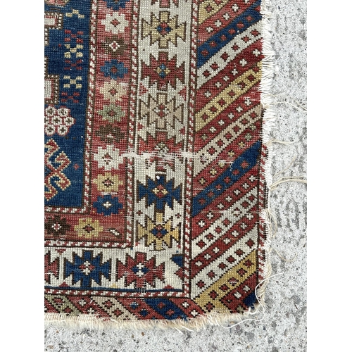 142 - An antique Caucasian rug, 100 by 114cms (wear and damages).