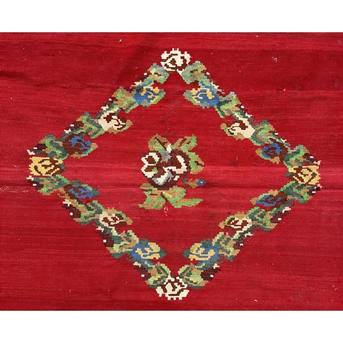 149 - A large Romanian kilim rug with floral motifs on a red ground within a repeating floral border, 310 ... 