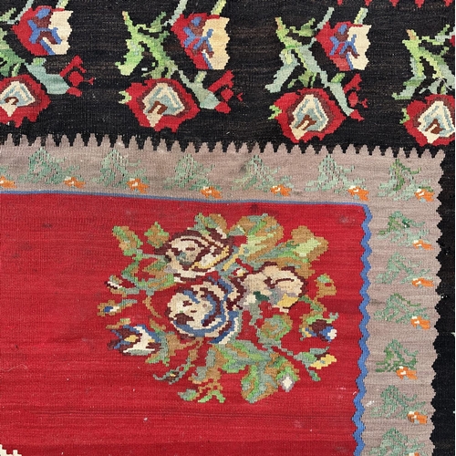 149 - A large Romanian kilim rug with floral motifs on a red ground within a repeating floral border, 310 ... 