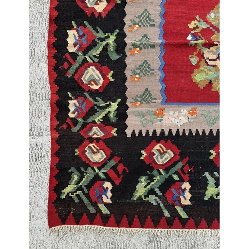 149 - A large Romanian kilim rug with floral motifs on a red ground within a repeating floral border, 310 ... 