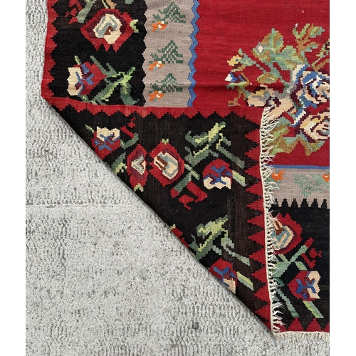 149 - A large Romanian kilim rug with floral motifs on a red ground within a repeating floral border, 310 ... 