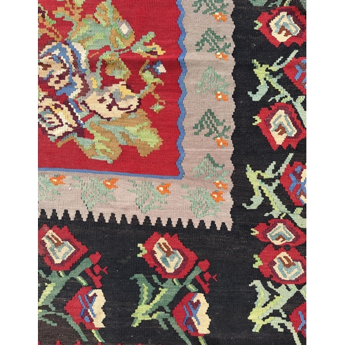 149 - A large Romanian kilim rug with floral motifs on a red ground within a repeating floral border, 310 ... 