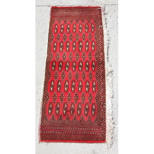 163 - A Persian Turkoman woollen hand-made small rug with geometric designs on a red ground, 124 by 54cms.