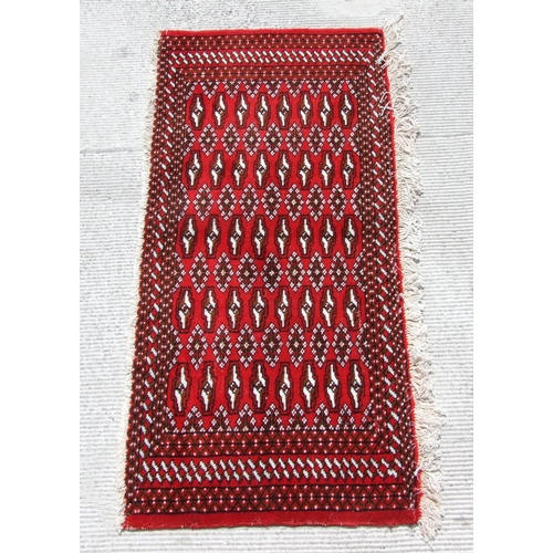 167 - A Persian Turkoman woollen hand-made small rug with geometric designs on a red ground, 126 by 58cms.