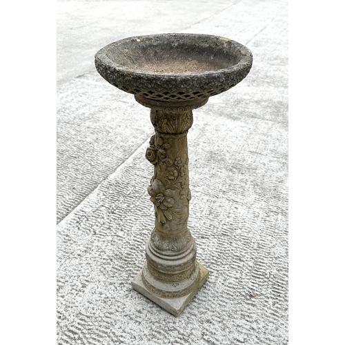 21 - A well weathered reconstitiuted stone bird bath, the column having rose decoration, 28cm diameter.