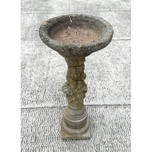 21 - A well weathered reconstitiuted stone bird bath, the column having rose decoration, 28cm diameter.