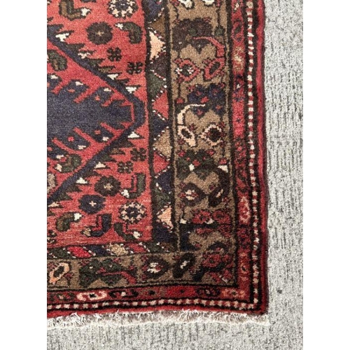 119 - A Persian Hamadan wool carpet with three central guls within geometric borders, on a red ground, 146... 