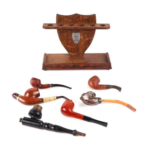 367 - A six division oak pipe rack with a selection of pipes to include a Black Forest style white metal e... 