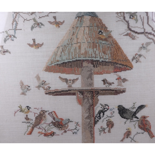 126 - A 20th century cross stitch embroidered panel depicting woodland birds on a bird feeder, framed & gl... 