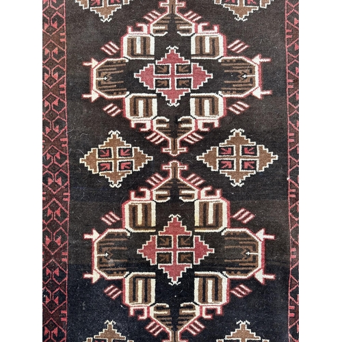 132 - A Persian rug with repeating geometric motifs on a black ground within a multi border, 113 by 215cms... 