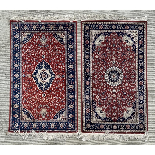 133 - A modern Persian rug decorated with foliate scrolls, on a red ground; together with another similar ... 