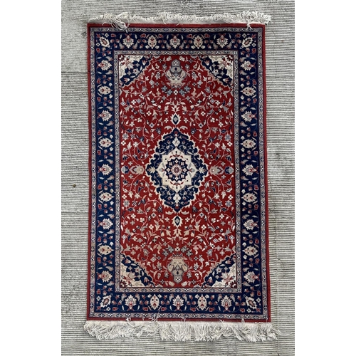 133 - A modern Persian rug decorated with foliate scrolls, on a red ground; together with another similar ... 