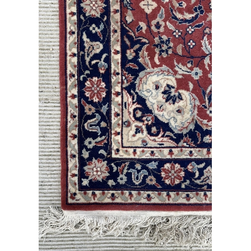 133 - A modern Persian rug decorated with foliate scrolls, on a red ground; together with another similar ... 