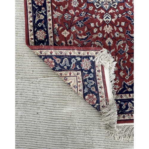 133 - A modern Persian rug decorated with foliate scrolls, on a red ground; together with another similar ... 