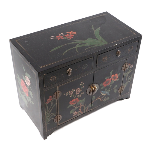 750 - A Chinese lacquer side cabinet with two frieze drawers above a cupboard, decorated with flower on a ... 