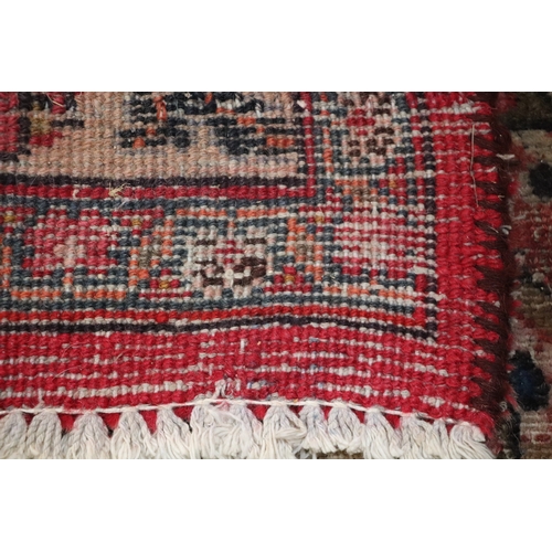 121 - A large Persian hand knotted woollen rug decorated with foliate scrolls, on a red ground, 310 by 330... 