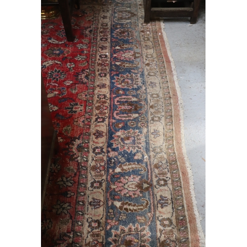 121 - A large Persian hand knotted woollen rug decorated with foliate scrolls, on a red ground, 310 by 330... 