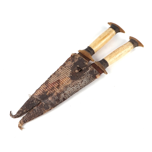 110 - A pair of African tribal daggers, having matching bone and horn hilts, twin double edged blades, and... 