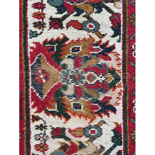 1371 - A Caucasian runner having a repeating floral design on a cream ground within a red and repeating geo... 